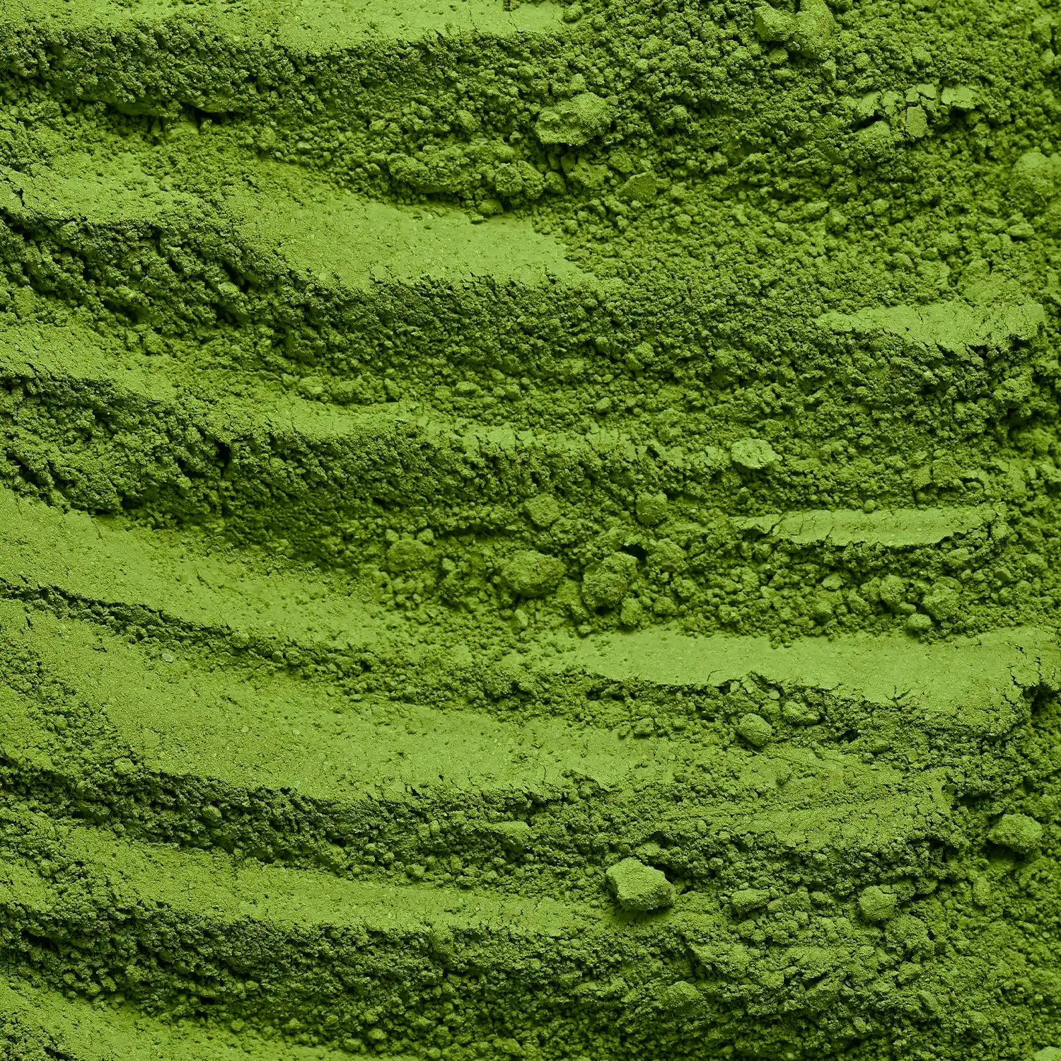 Close-up texture of bright green powder with horizontal ridges and small clumps, filling the entire frame.